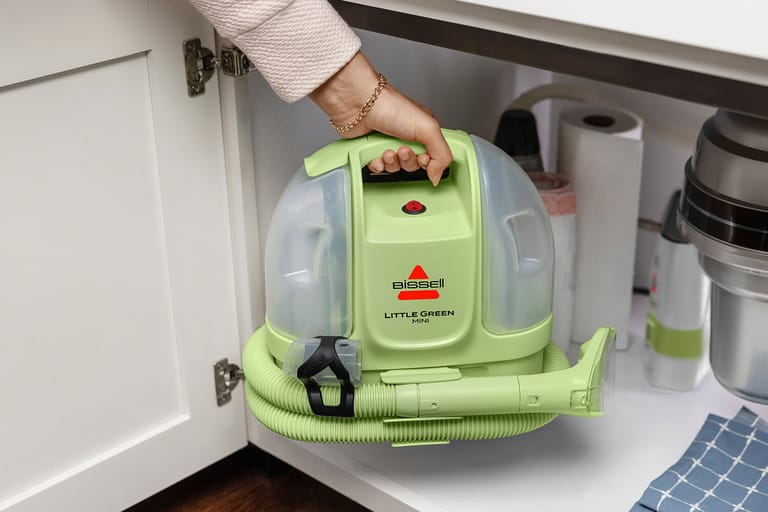 Tea Green Little Green Mini with its hose wrapped around the base being placed in a cabinet.